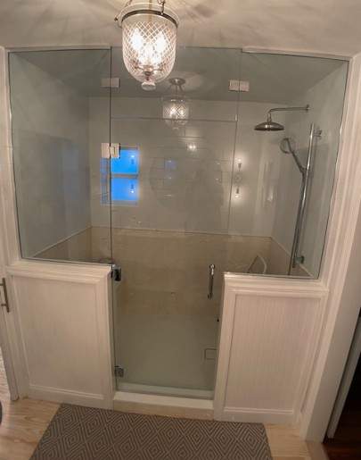 Walk-in shower with glass walls and light fixture hanging outside of the enclosure